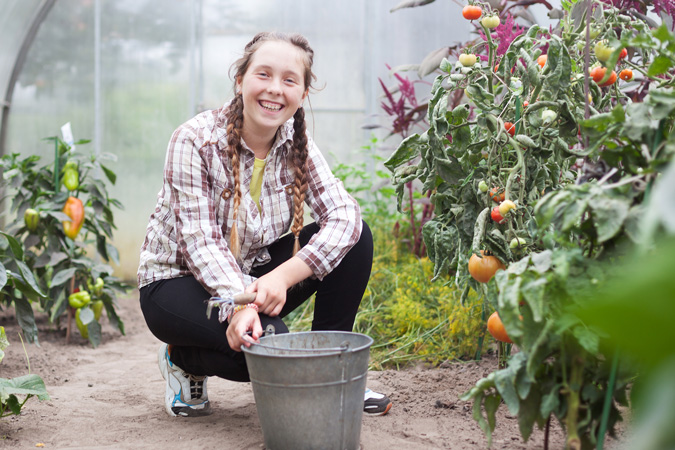 Student in greenhouse smiling  surrounded by fresh grown vegetables 